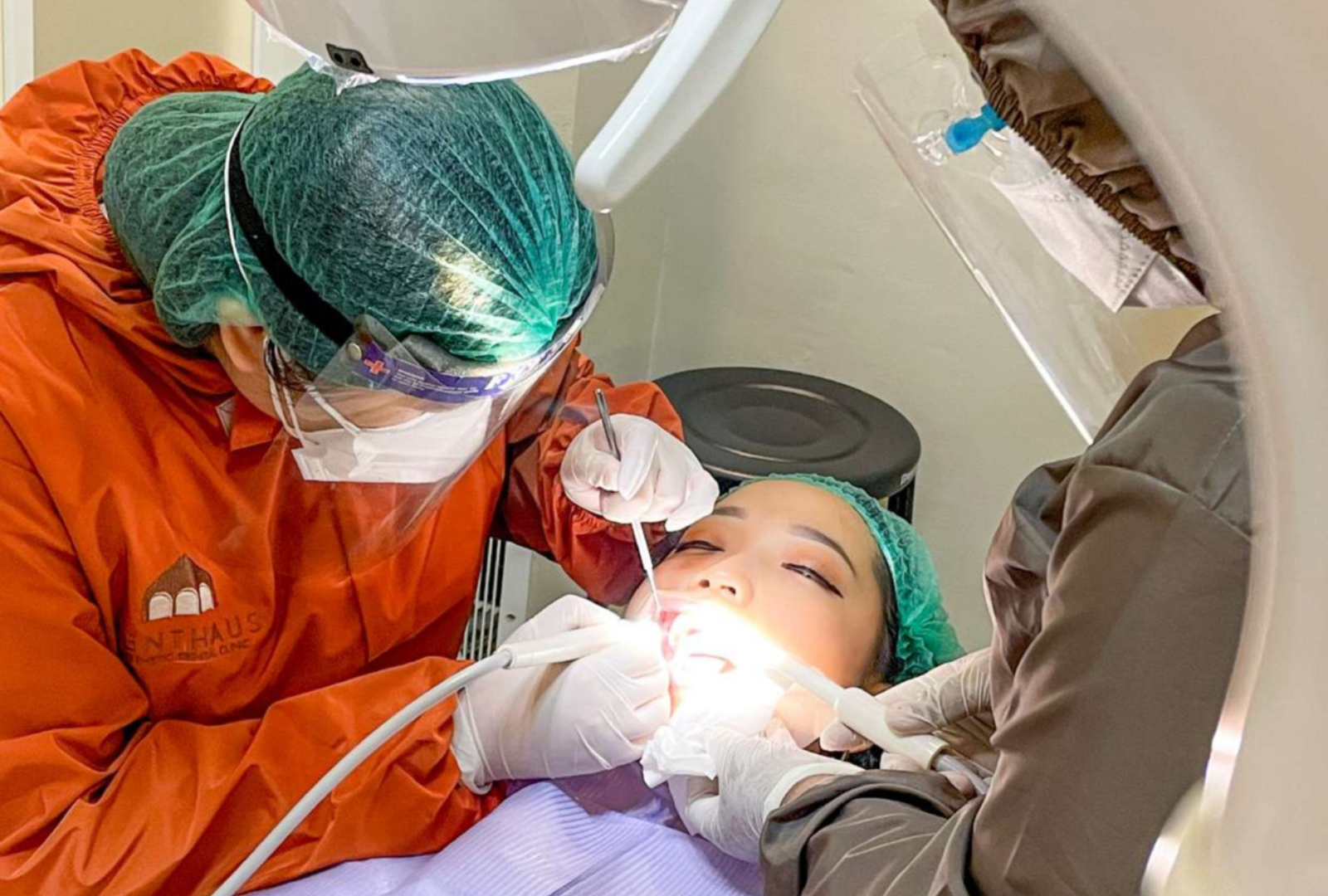 Dokter gigi Denthaus melakukan tindakan perawatan pasien dari sisi kursi dental.